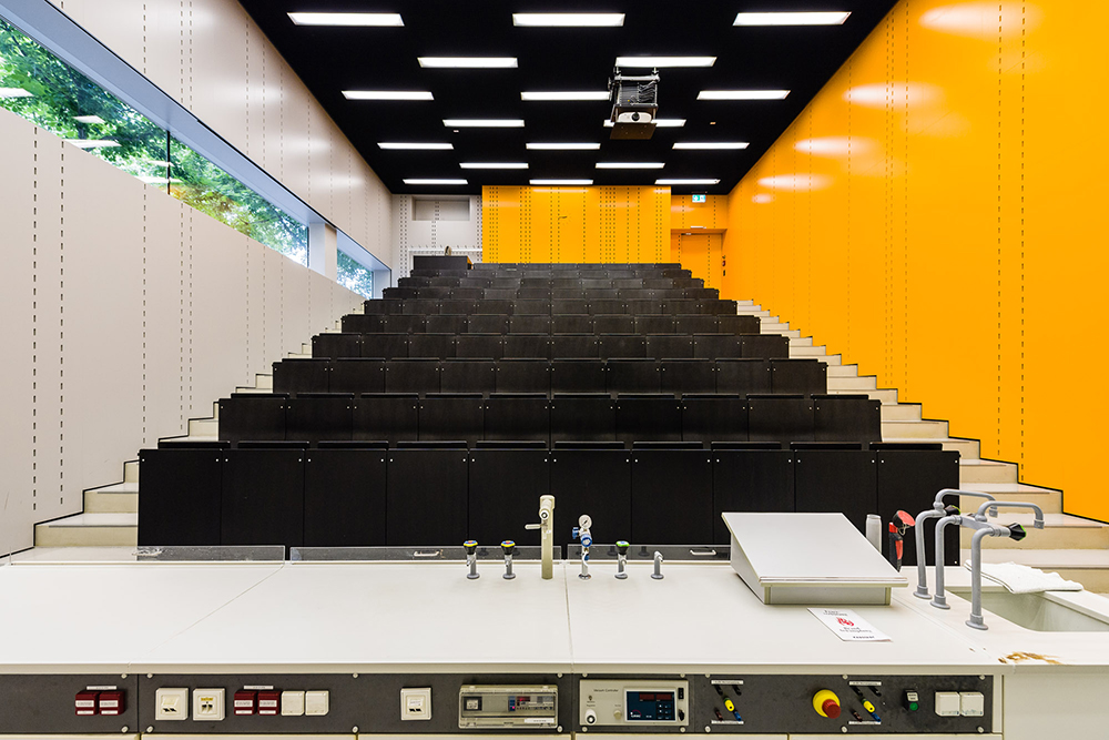 Hörsaal mit schwarzen Stühlen und oranger Wand im Naturwissenschaftlichen Gebäude