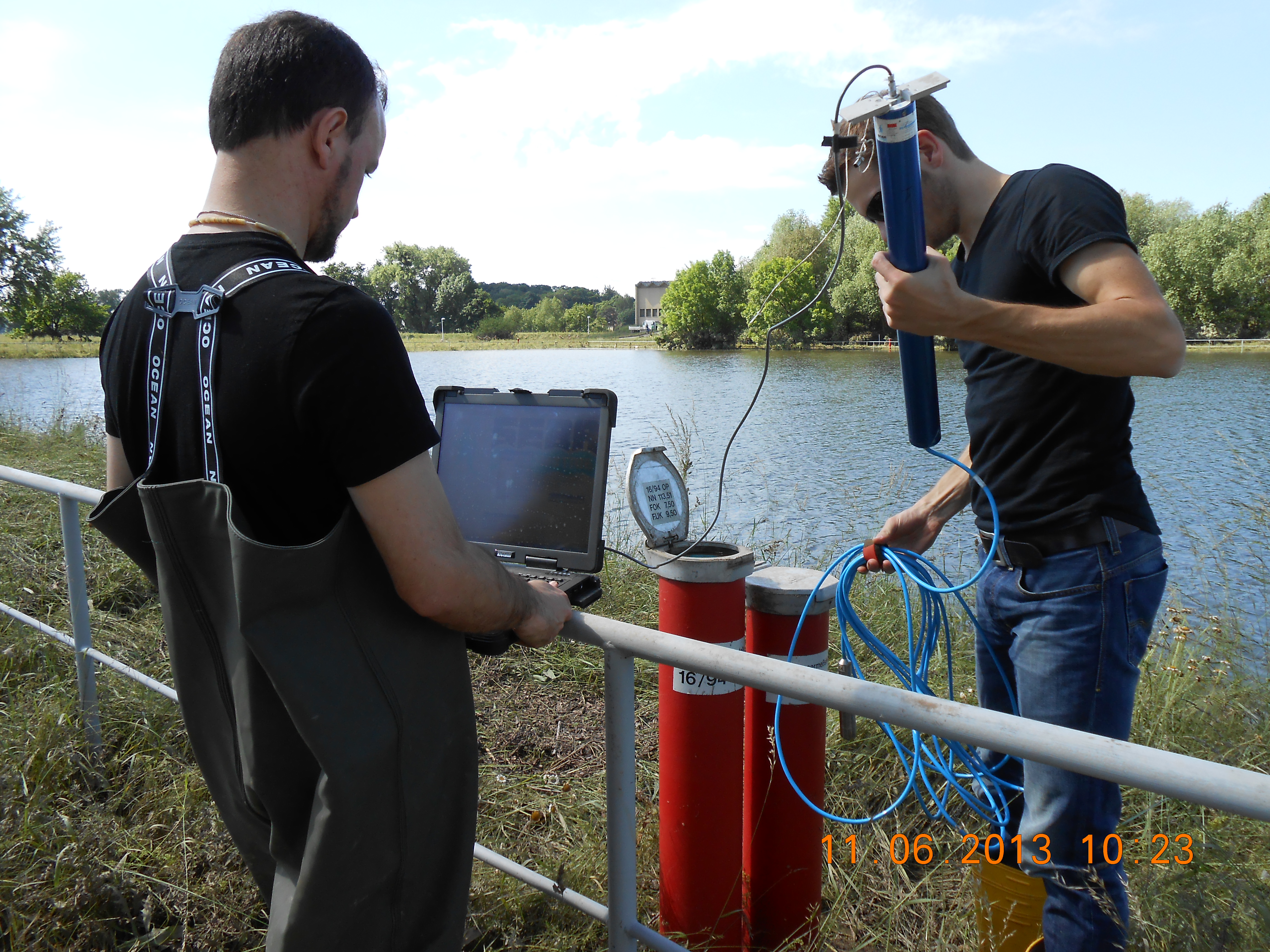 Two person installing equipement in a monitoring well, background river