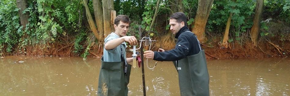 Mann steht während Probenahme im eisenhaltigen Fluss mit Wathose