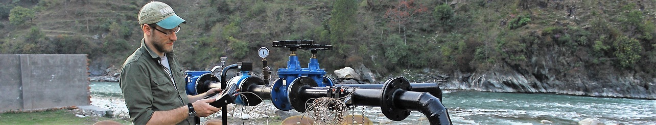 Mann steht vor Rohrleitung und führt Messungen durch, im Hintergrund Gebrigsfluss