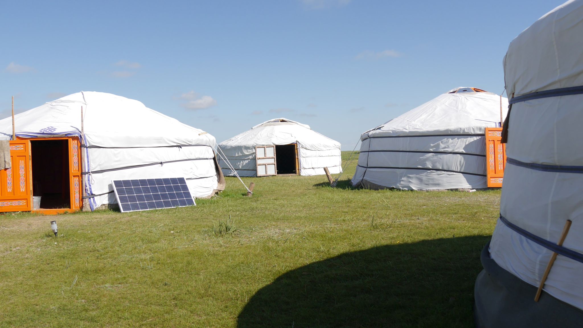 Ein Bild, das mehrere mongolische Jurten und etwas Ausrüstung, wie ein Solarpanel zeigt.