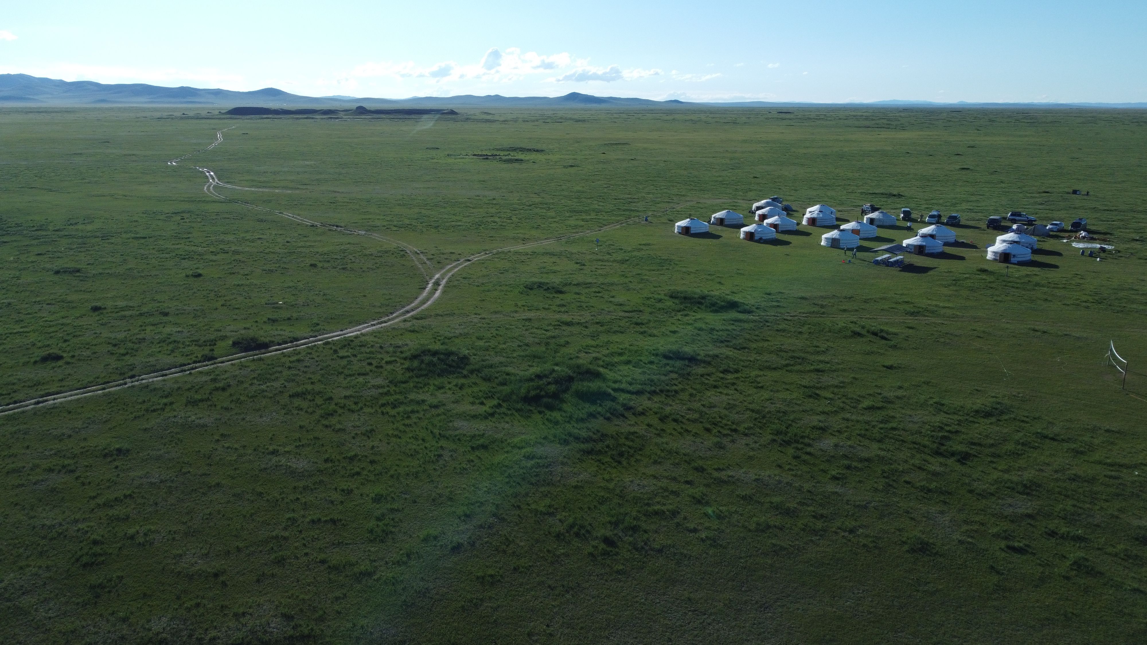 Das Bild zeigt eine Steppenlandschaft im Hintergrund sind die Ruinen einer alten Stadt zu sehen, im Vordergrund ein Camp aus zahlreichen mongolischen Jurten