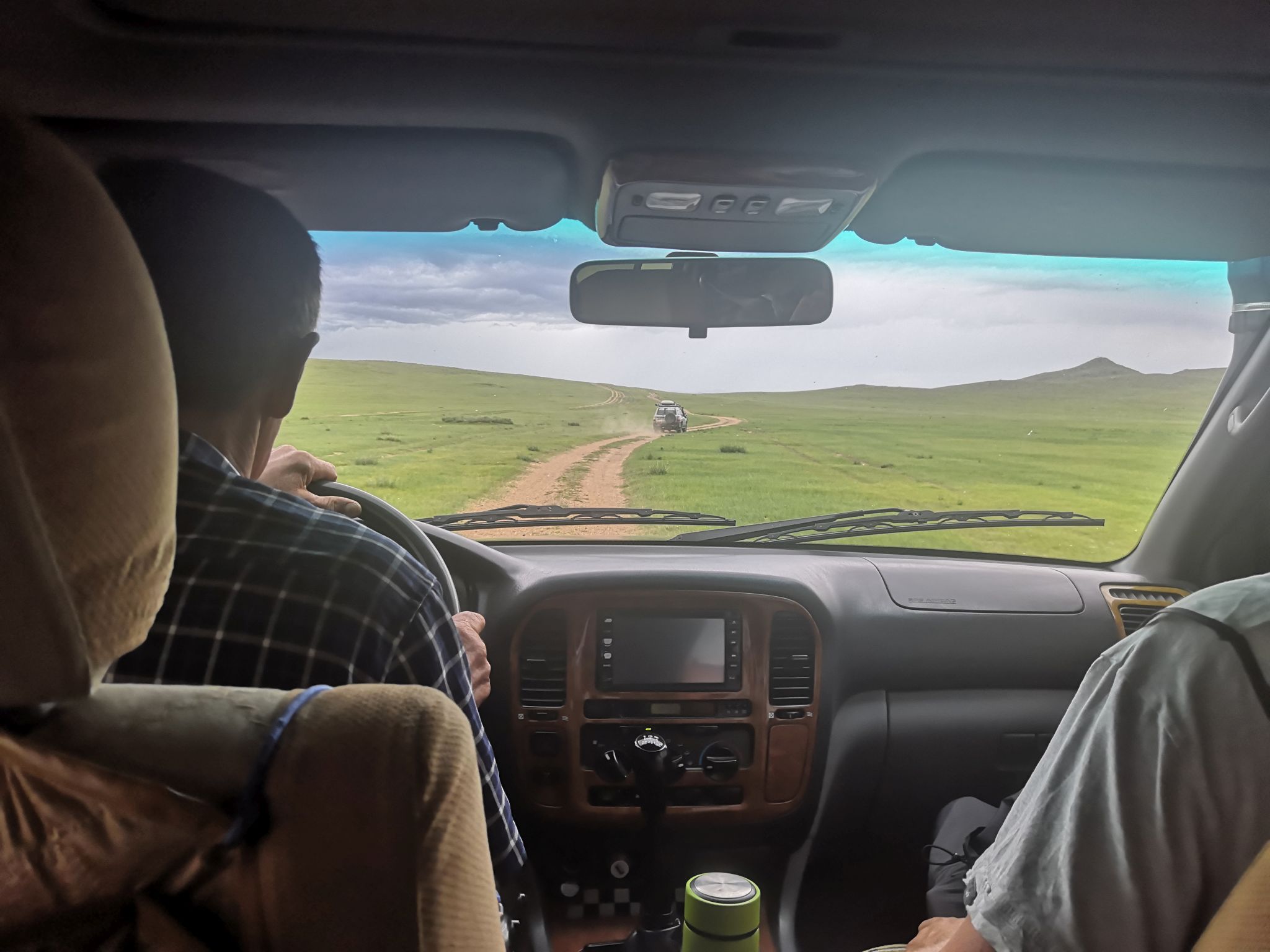 Das Bild zeigt das Cockpit eines Geländewagens. Durch die Windschutzscheibe ist die mongolische Steppe und eine Piste bis zum Horizont zu sehen.