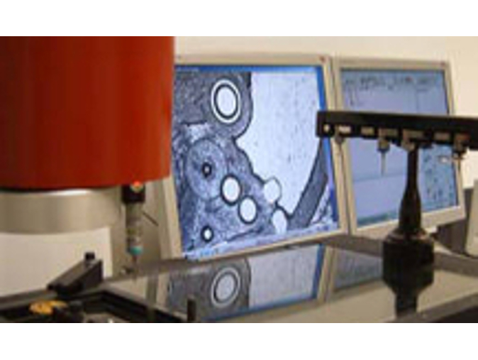 Das Bild zeigt die optische Antastung einer Uhrenplatine mit dem optischen Sensor eines Koordinatenmessgeräts, im Hintergrund ist eine Tasterwechselbank zu sehen.