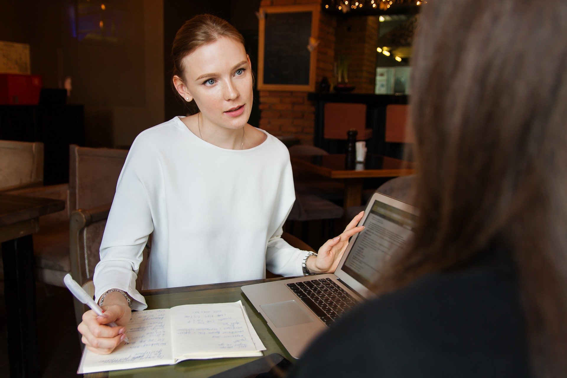 Beratungssituation, zwei Frauen sich gegenüber sitzend im Gespräch, Schreibunterlagen und Laptop auf dem Tisch