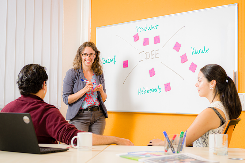 Eine Gründugsberaterin erklärt an einem Whiteboard die Grundlagen der Ideenfindung