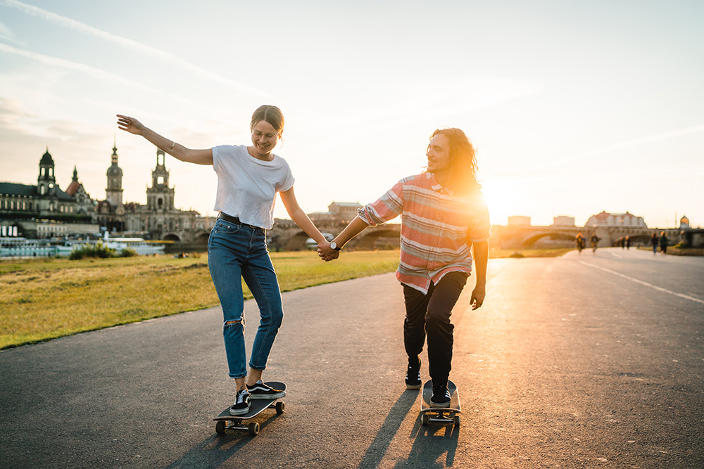 Zwei junge Menschen skaten auf dem Elbradweg vor der Altstadtkulisse Dresdens