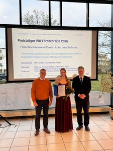 Frau Naumann mit zwei ihrer Betreuer vor einer Plaketwand mit dem Thema ihrer Abschlussarbeit, seitlich fotografiert