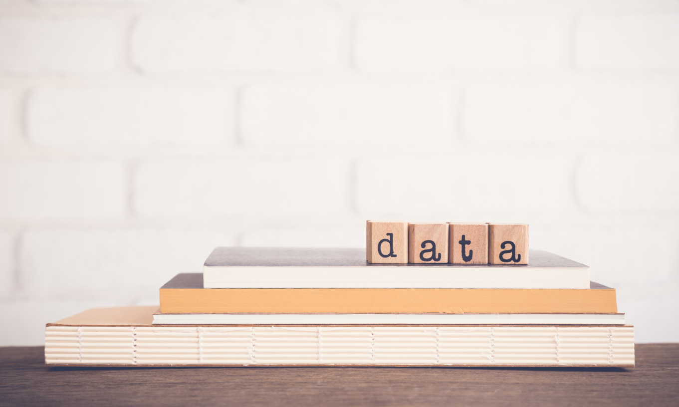 Die vier Buchstaben D, A, T und A stehen als Holzwürfel auf einem Bücherstapel und bilden das Wort Data.