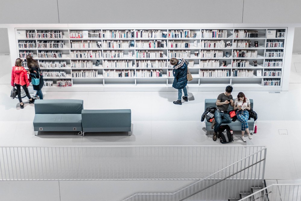 Von der oberen Etage in eine Bibliothek fotografiert. Menschen sitzen auf Sitzgelegenheiten und lesen.