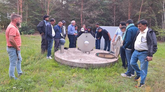 Personen stehen auf einer Wiese vor einem Brunnen