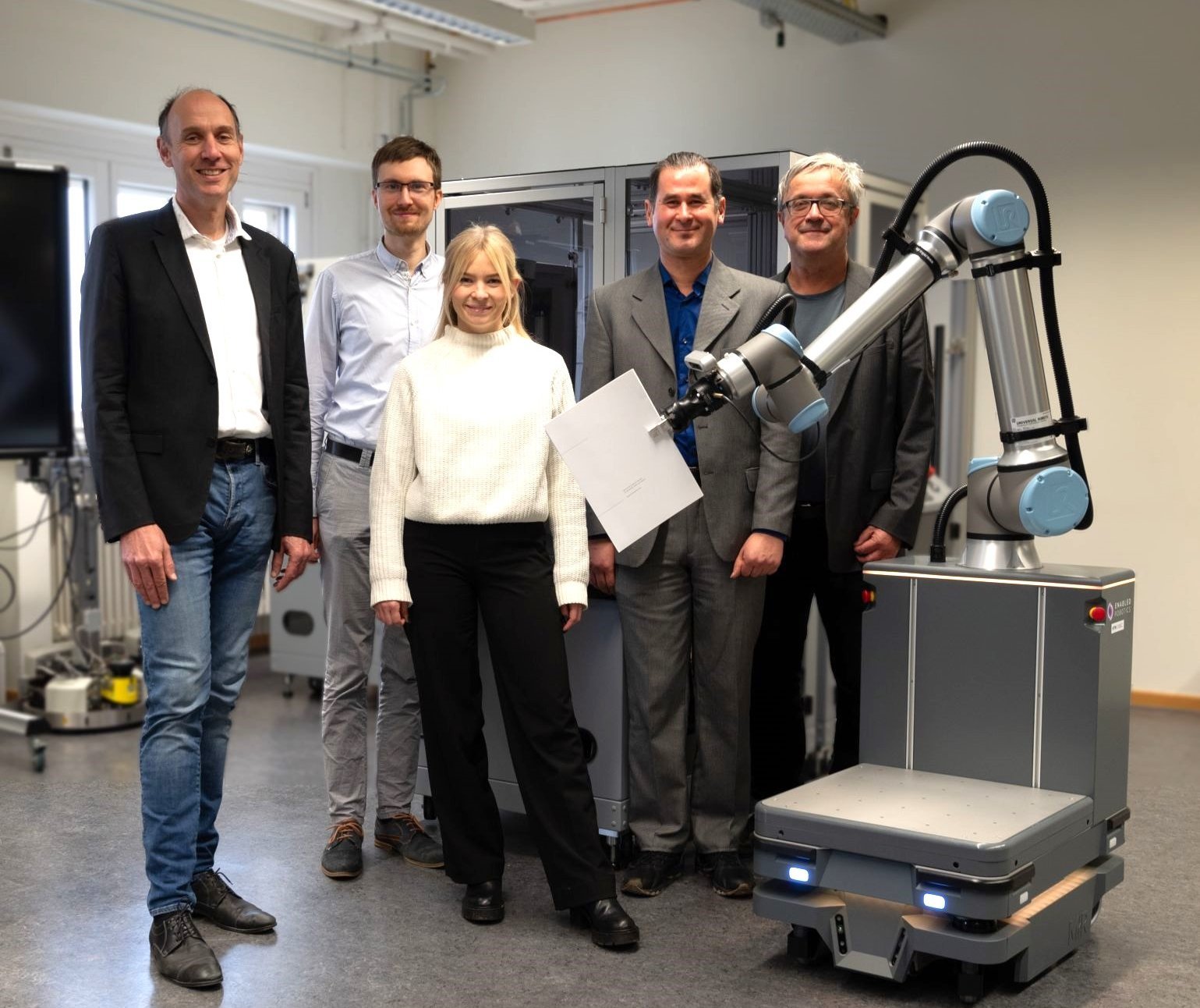 Projektmitarbeiter gemeinsam mit Cobot und Fördermittelbescheid