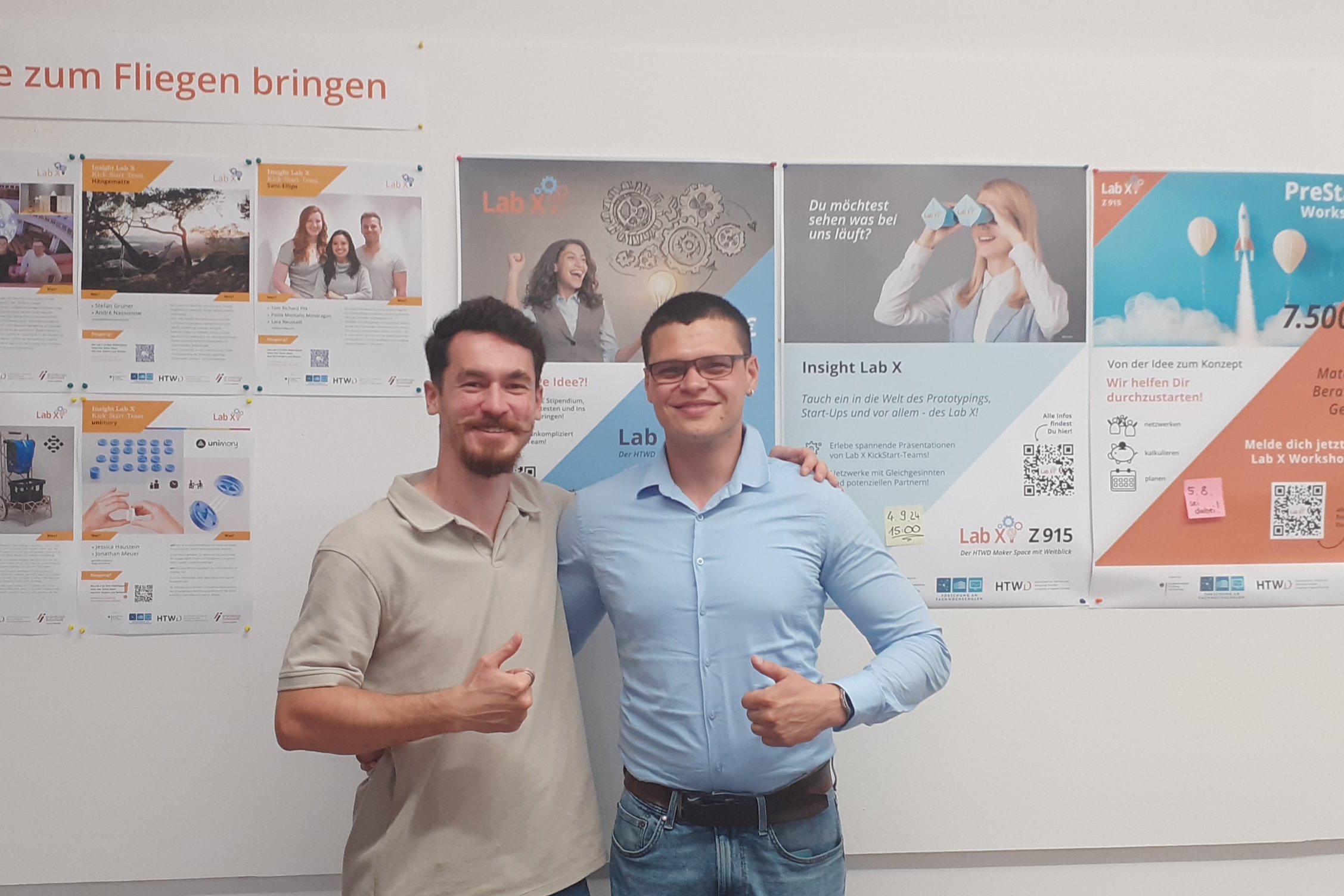 Zwei Männer stehen vor einer Plakatwand des Lab X