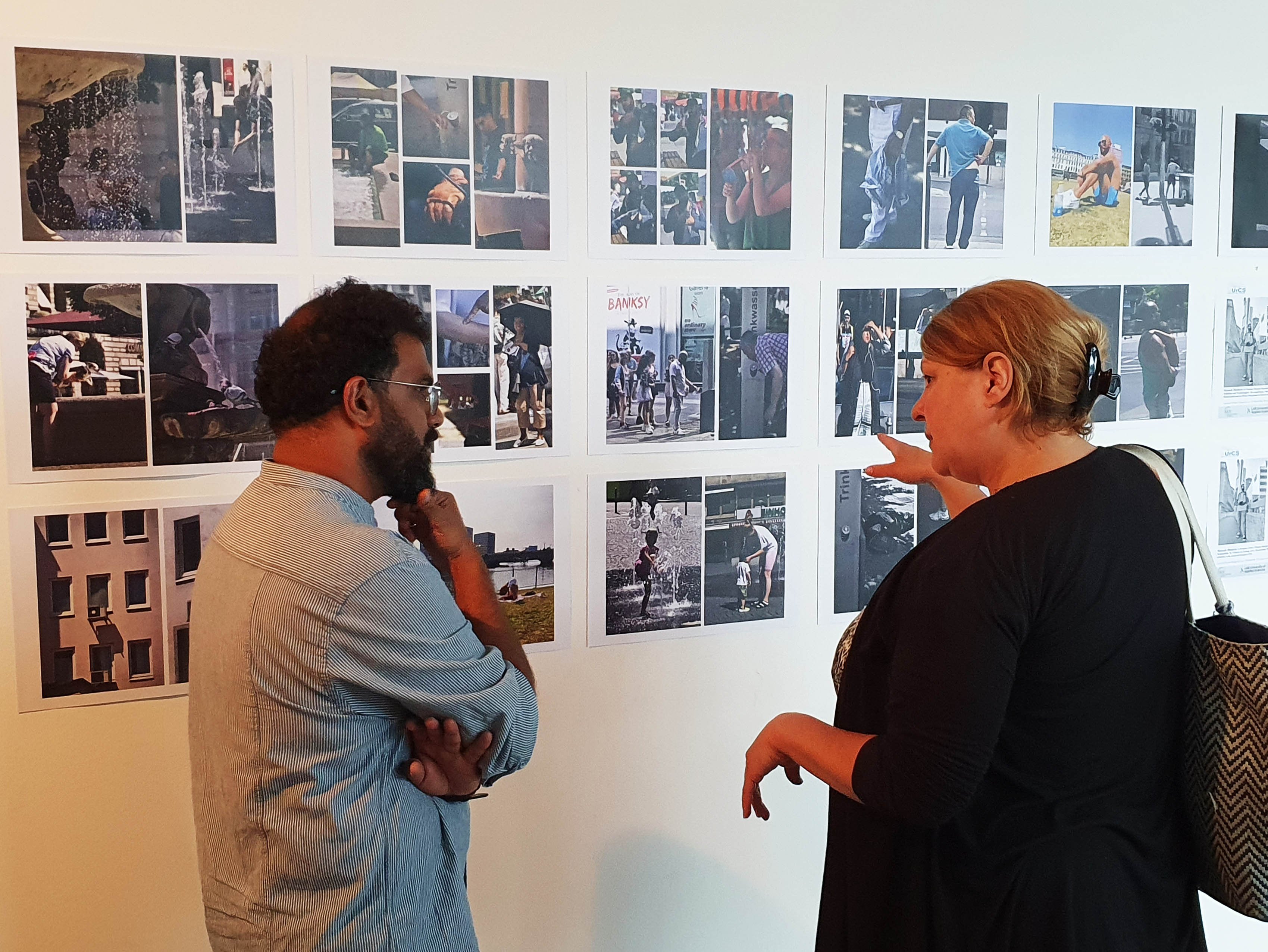 [Translate to English:] Ein Mann und eine Frau stehen vor einer Wand mit Fotos