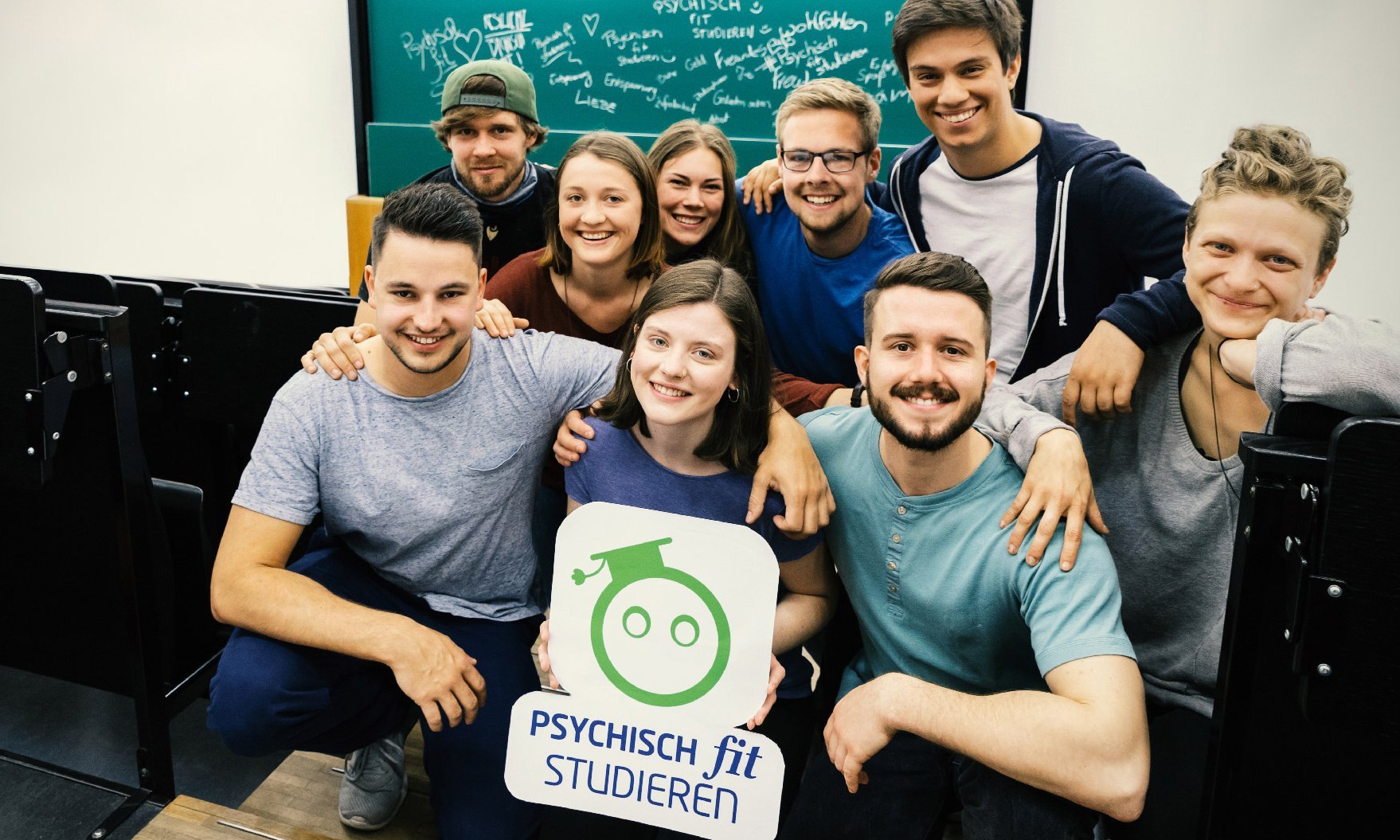 Gruppe Studierender hält Logo-Plakat Psychisch fit studieren hoch