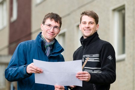 Zwei Männer stehen mit einem Plan vor einem Gebäude