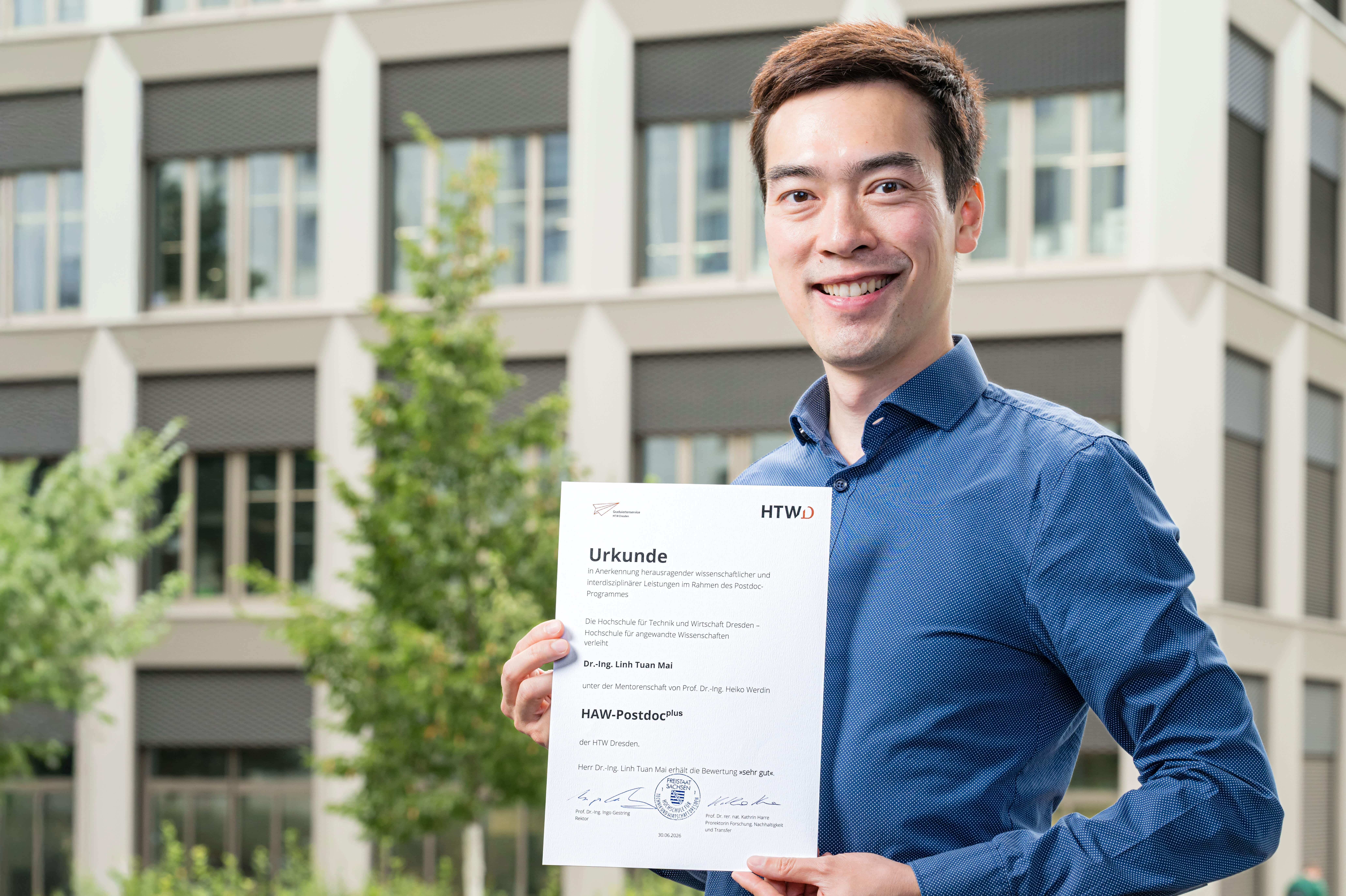Mann mit Urkunde für Postdoc vor einem Gebäude