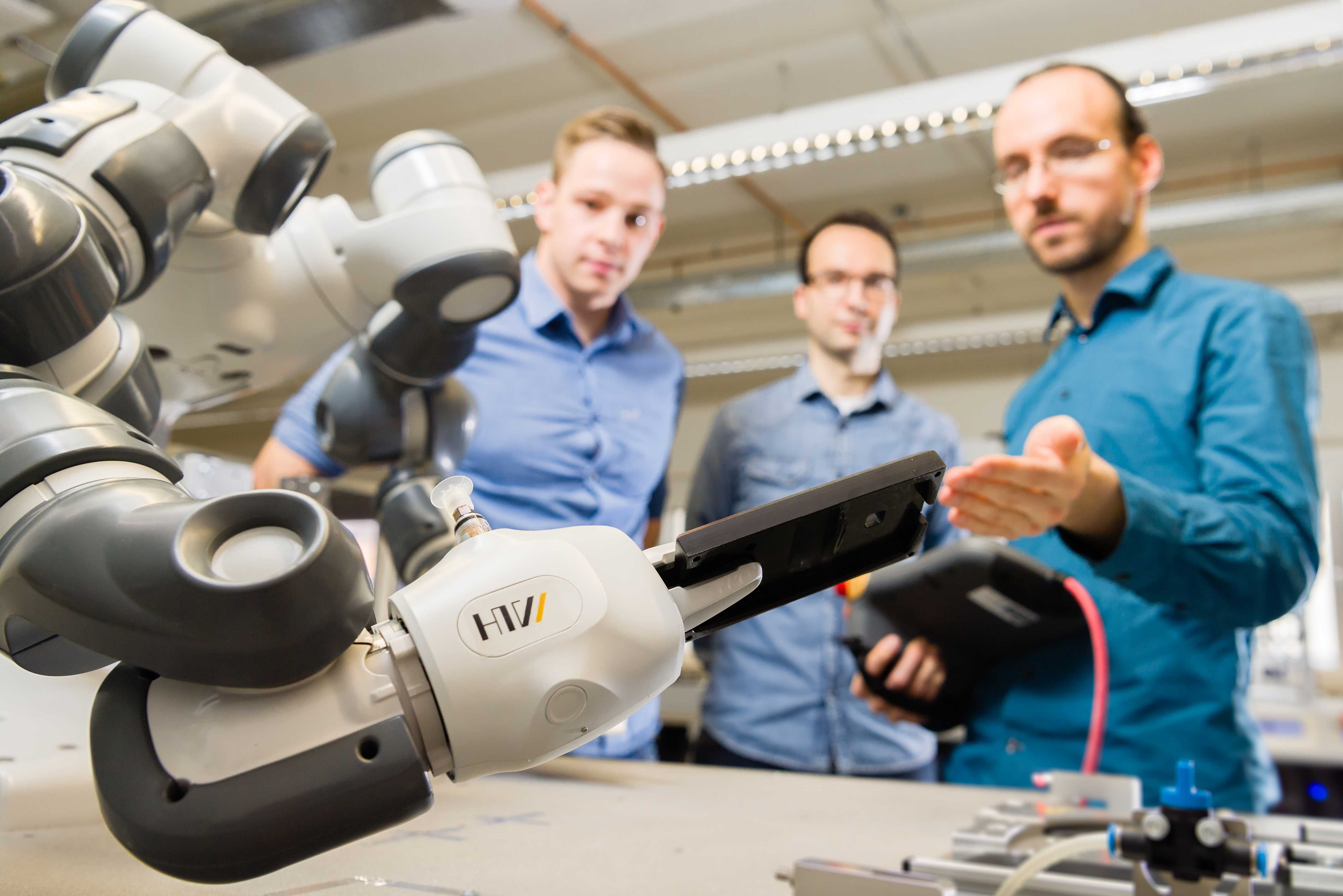 Collaborative robot in the foreground holds a housing bottom shell, employee in the background controls the robot