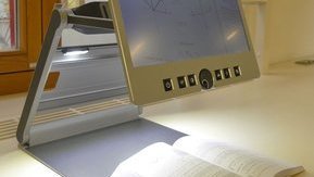 [Translate to English:] Ein Bildschirmlesegerät wird an einem Tisch zum Buch lesen verwendet