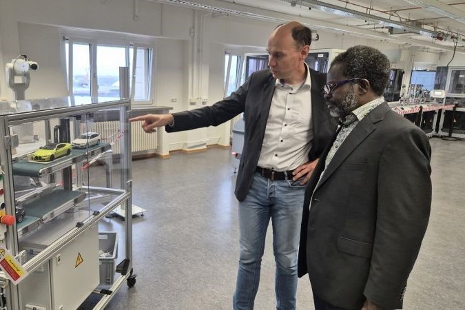 Zwei Männer stehen in einer Fabrikumgebung und unterhalten sich über das was sie umgibt