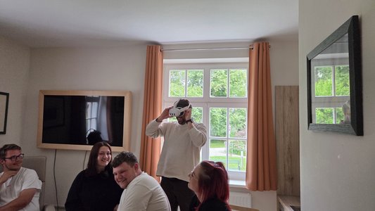 Pflegekraft beim Ausprobieren einer Augmented-Reality-Brille vor anderen sitzenden Pflegekräften