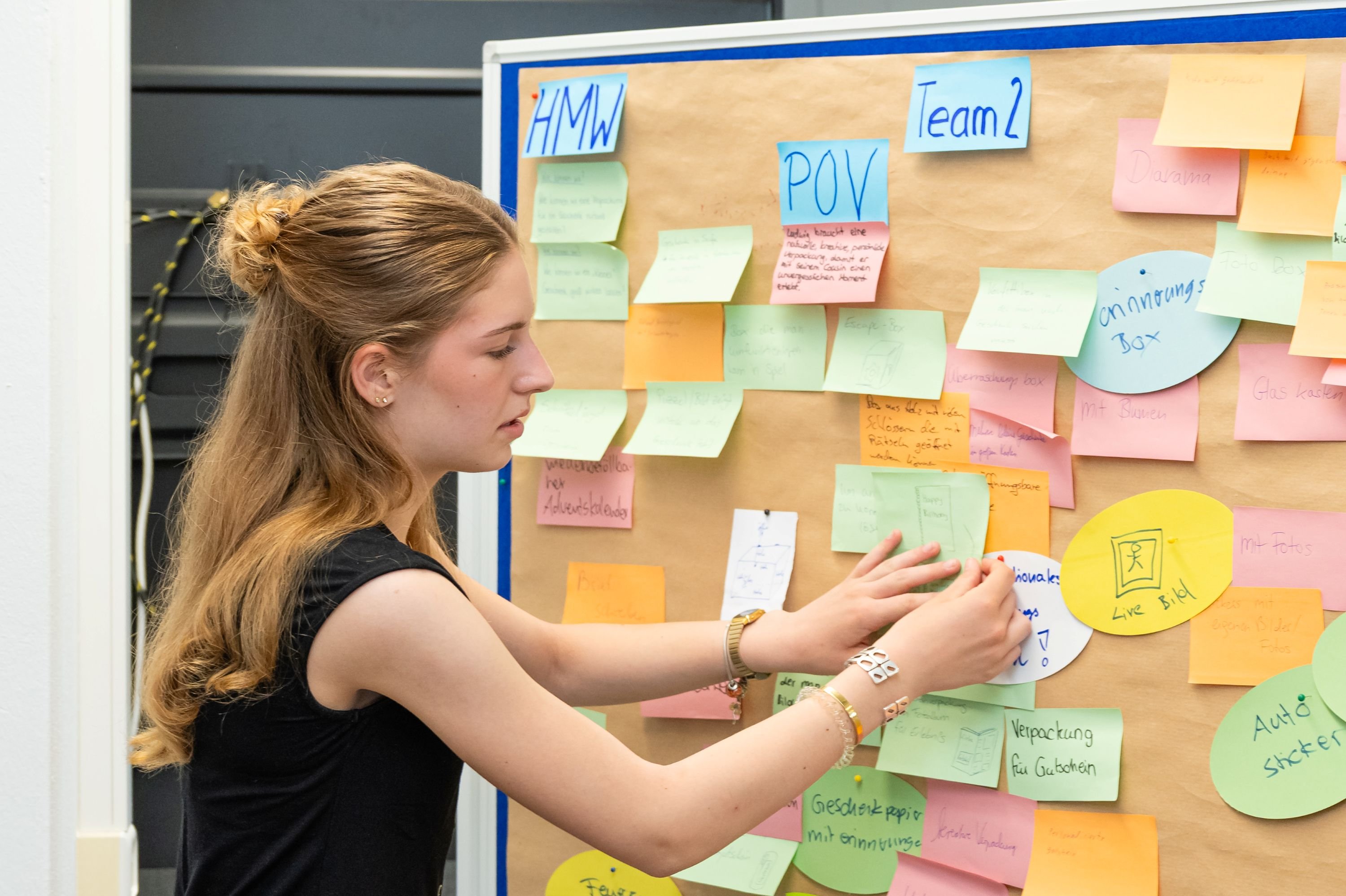 Junge Frau klebt Zettel mit Ideen an eine Pinwand