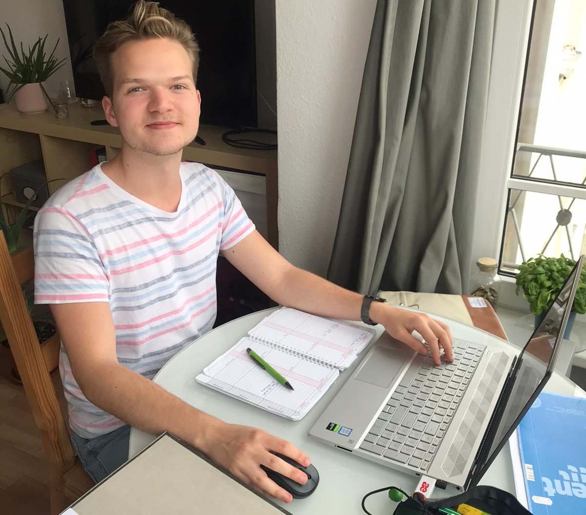 Foto; Student Thomas Pleiß sitzt im HomeOffice an seinem Schreibtisch vor einem Laptop. Er hält mi der einen Hand die Computermaus fest.