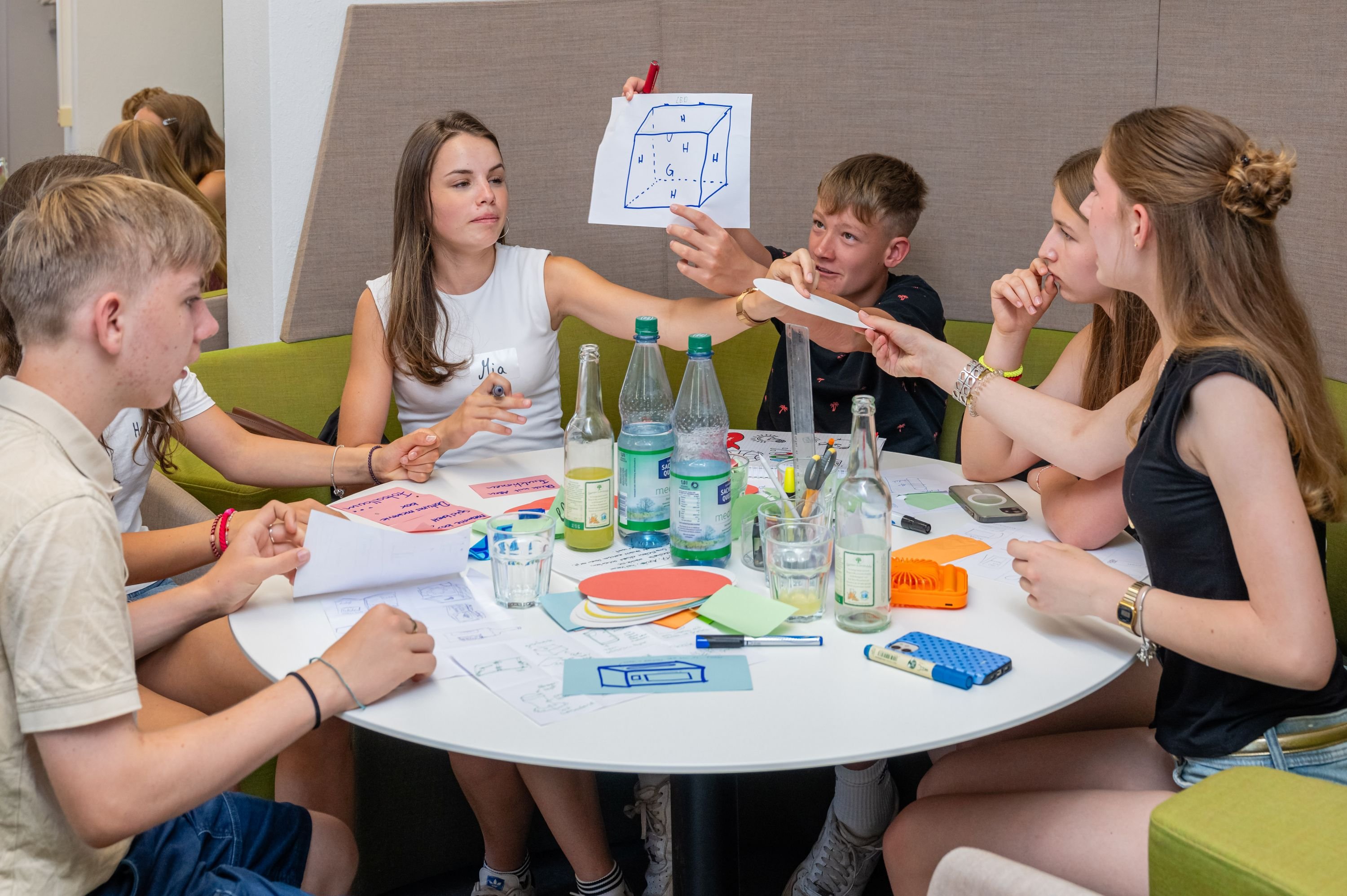 eine Gruppe von Jungendlichen sitzt um einen runden Tisch und arbeitet gemeinsam  Ideen aus