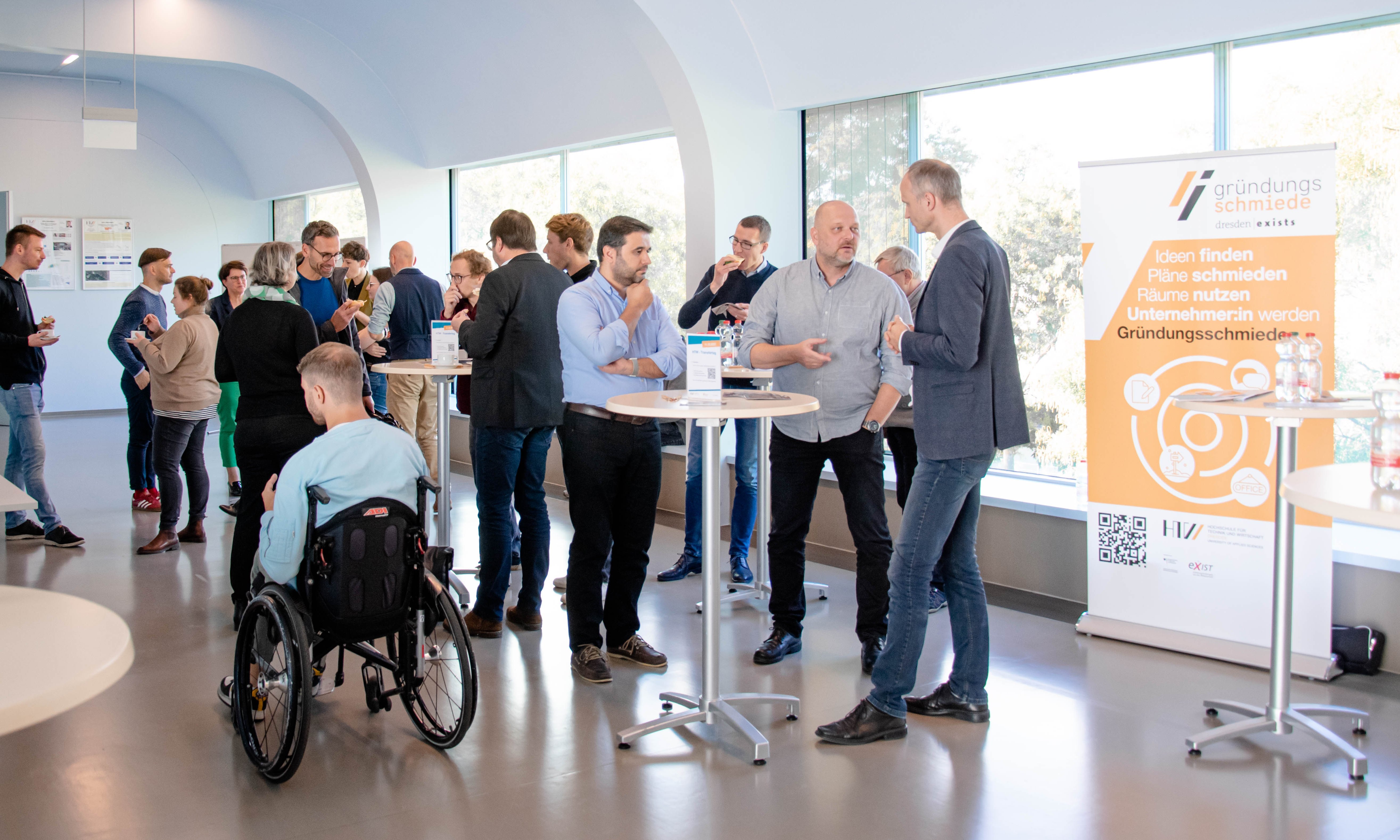 Schnappschuss der Teinehmenden vom Transfertag 2022; Gruppe von Menschen steht um Stehttische verteilt und unterhält sich