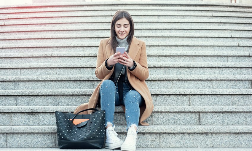 Frau sitzt auf Treppenstufen und schaut auf ihr Mobiltelefon