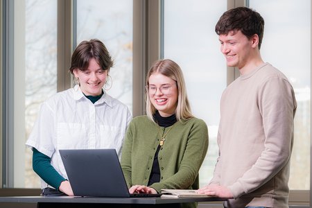 Luisa Rengers, Seline Rühle und Christian Redlich stehen vor einem Laptop zur Fallbeispielbearbeitung