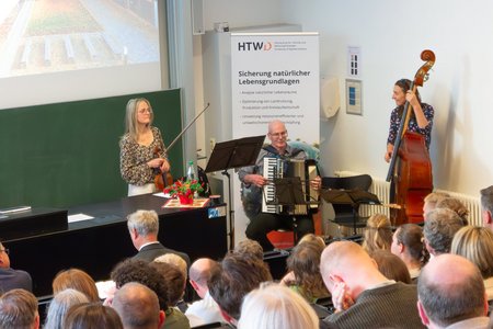 Drei Musiker*innen, die vor einem Publikum stehen.