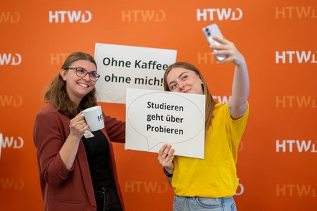 zwei Frauen vor HTWD-Hintergrund mit Handy in der Hand