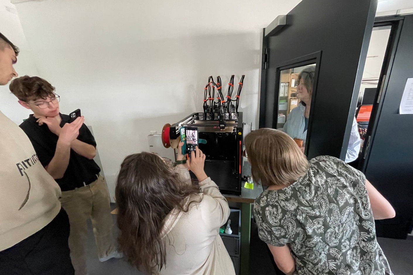 einige Menschen schauen interessiert dem 3D-Drucker bei der Arbeit zu und filmen dies