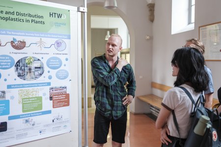 Ein, Mann der neben einem Poster steht und mit zwei Menschen spricht.