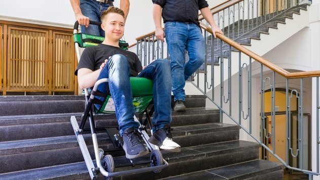 ein Mann wird in einem Evakuierungsstuhl von einem weiteren Mann die Treppe heruntergefahren