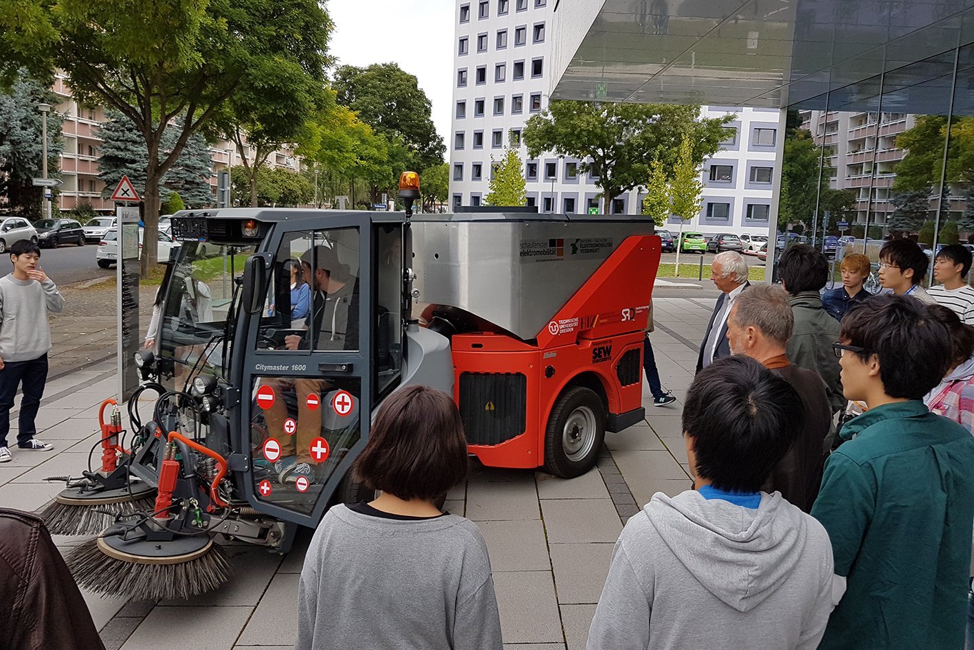 [Translate to English:] Studierende aus Japan stehen vor einer Kerhmaschine