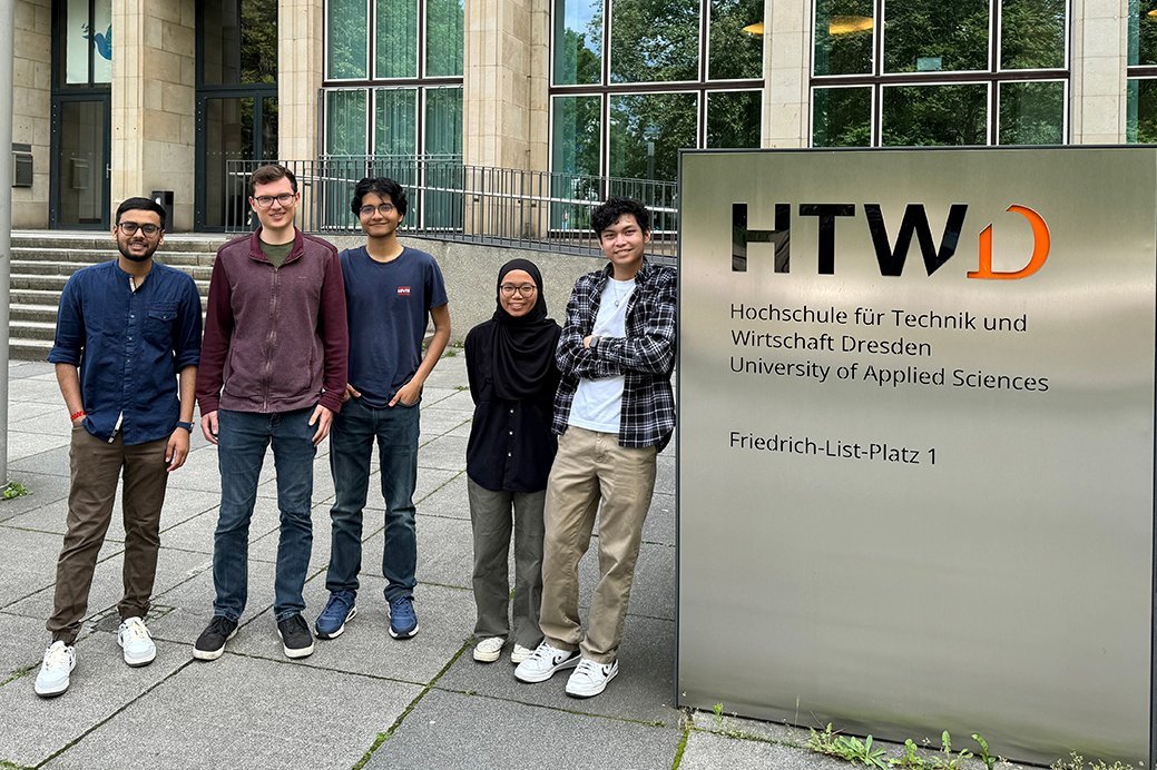 Eine Gruppe Studierende steht vor dem Haupteingang der HTWD und blickt erfreut in die Kamera