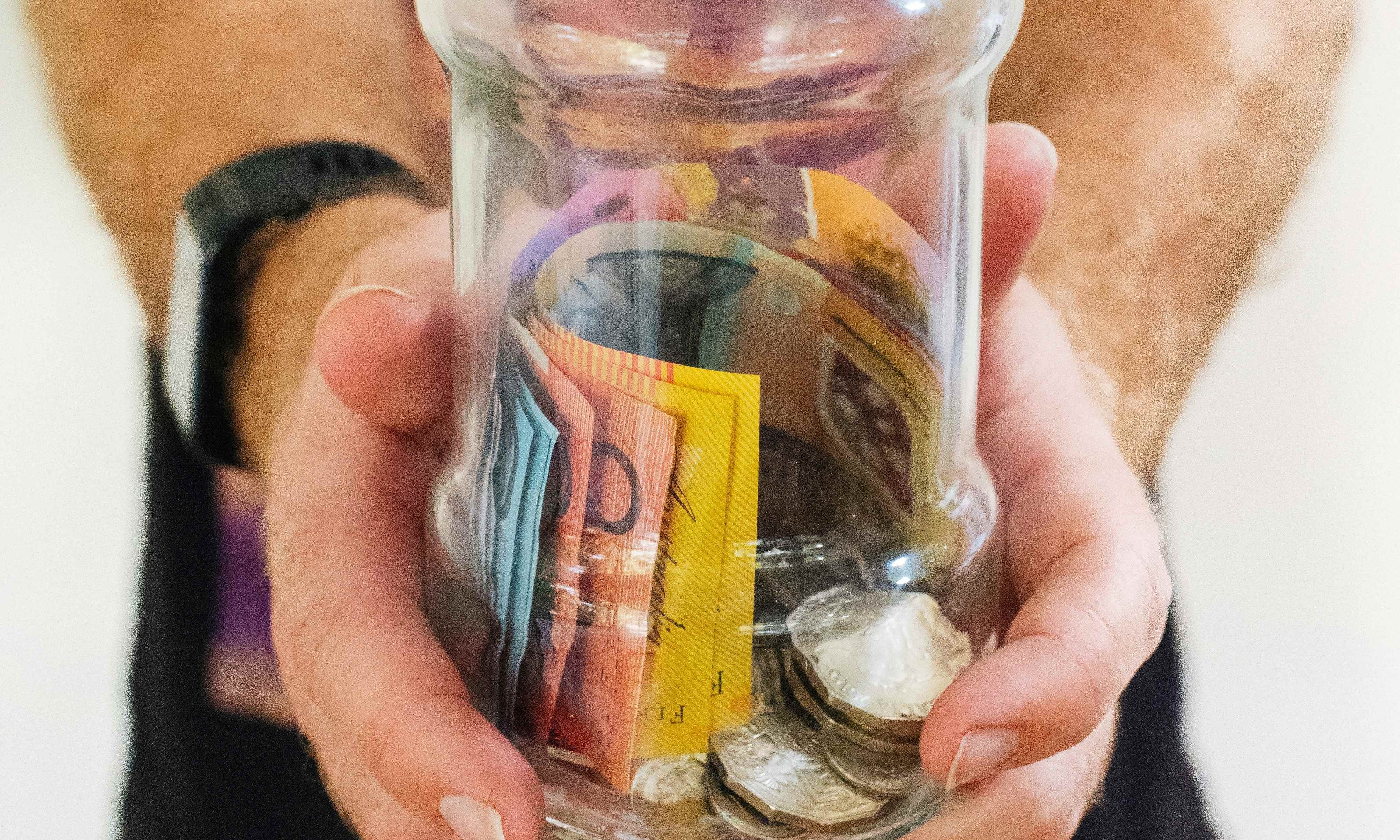 Hände mit einem Glas voller Münzen und Scheine