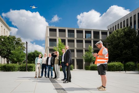 Eine Menschengruppe steht auf dem Campusplatz der HTWD und schaut in den Himmel, wo eine Drohne fliegt